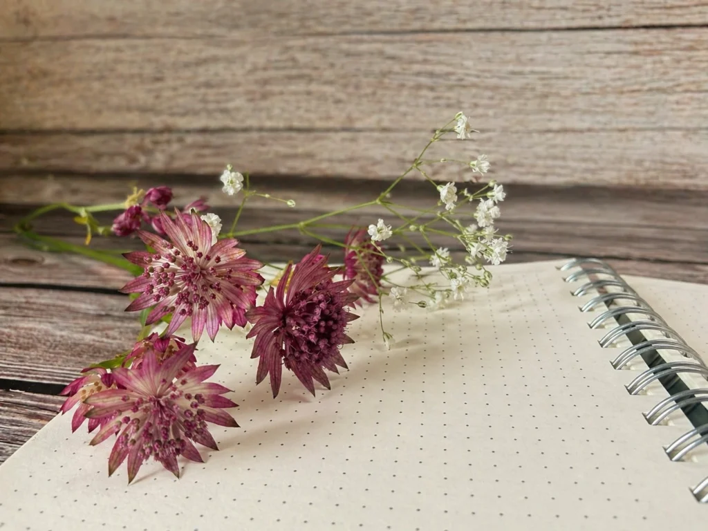 Leeres Notizbuch mit gepunkteten Seiten und Blumen auf einem Holztisch – Journaling am Abend vorbereiten