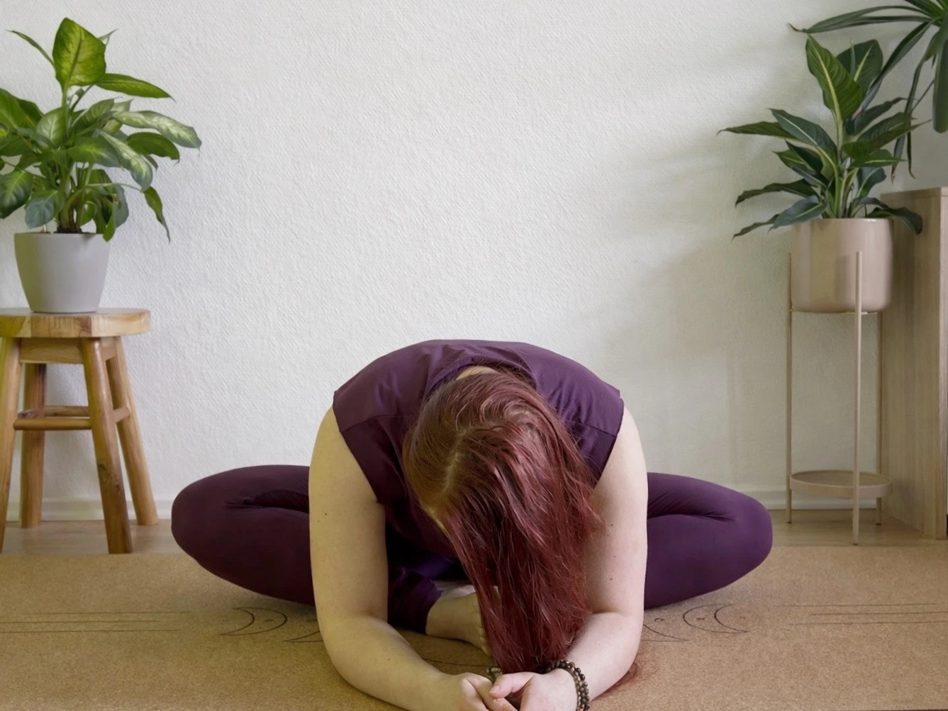 Frau in Yin Yoga Schmetterling (Baddha Konasana) auf einer Matte, Oberkörper nach vorne gebeugt, ruhige Innenraum-Atmosphäre mit Pflanzen