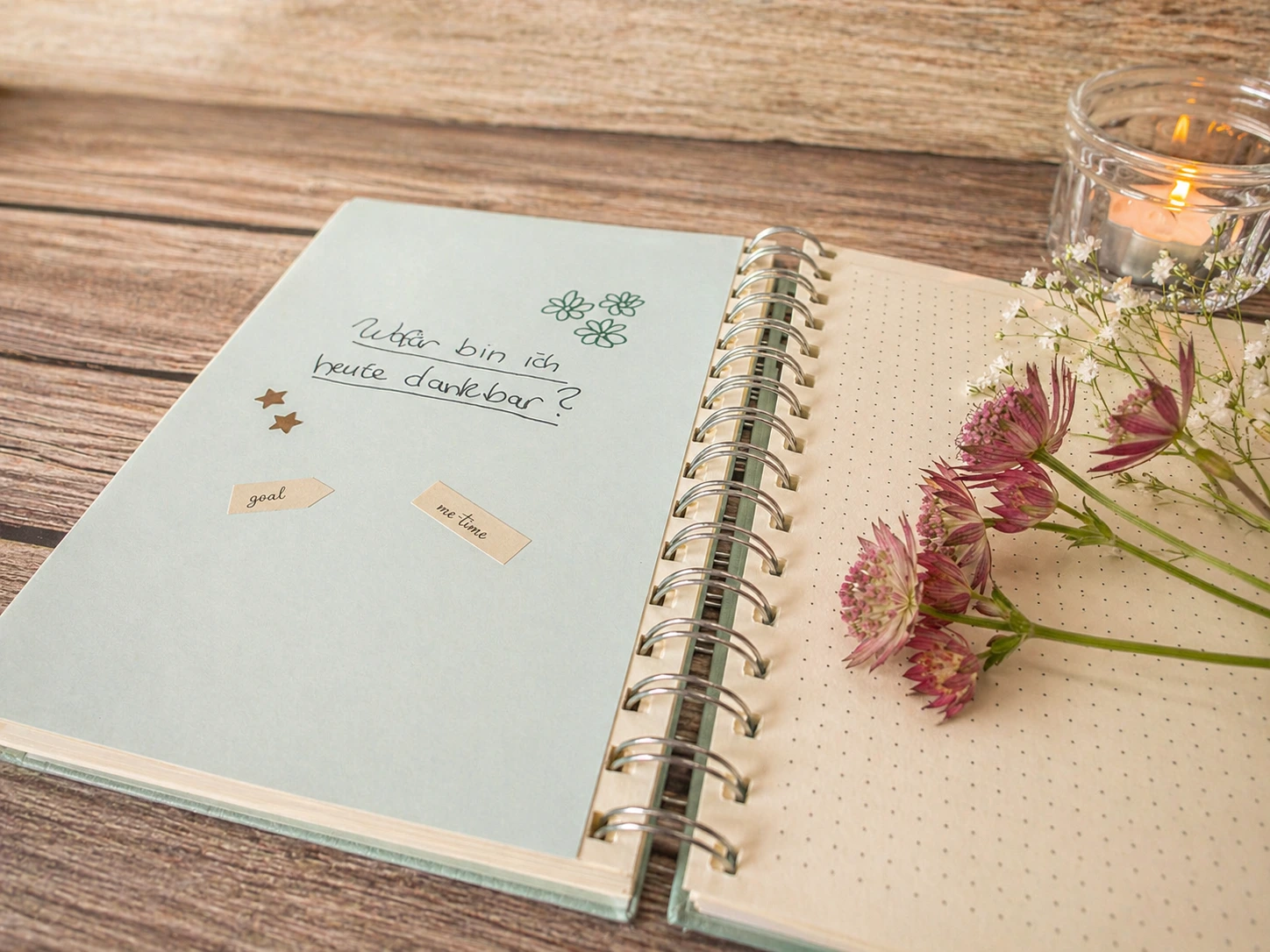 Offenes Notizbuch mit Journaling-Frage „Wofür bin ich heute dankbar?“, Blumen und Kerze auf Holztisch