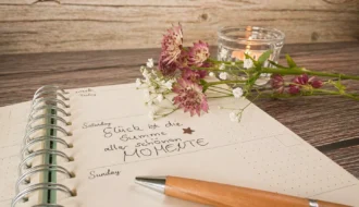 Journaling am Abend: Notizbuch, Stift, Blumen und Kerze auf einem Holztisch