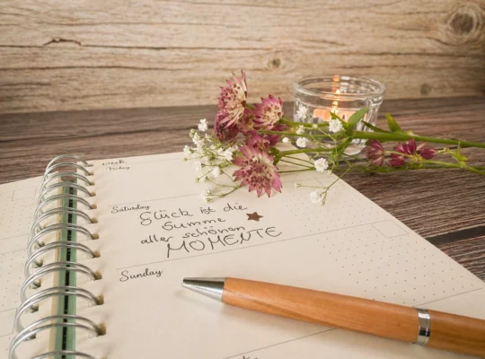 Journaling am Abend: Notizbuch, Stift, Blumen und Kerze auf einem Holztisch