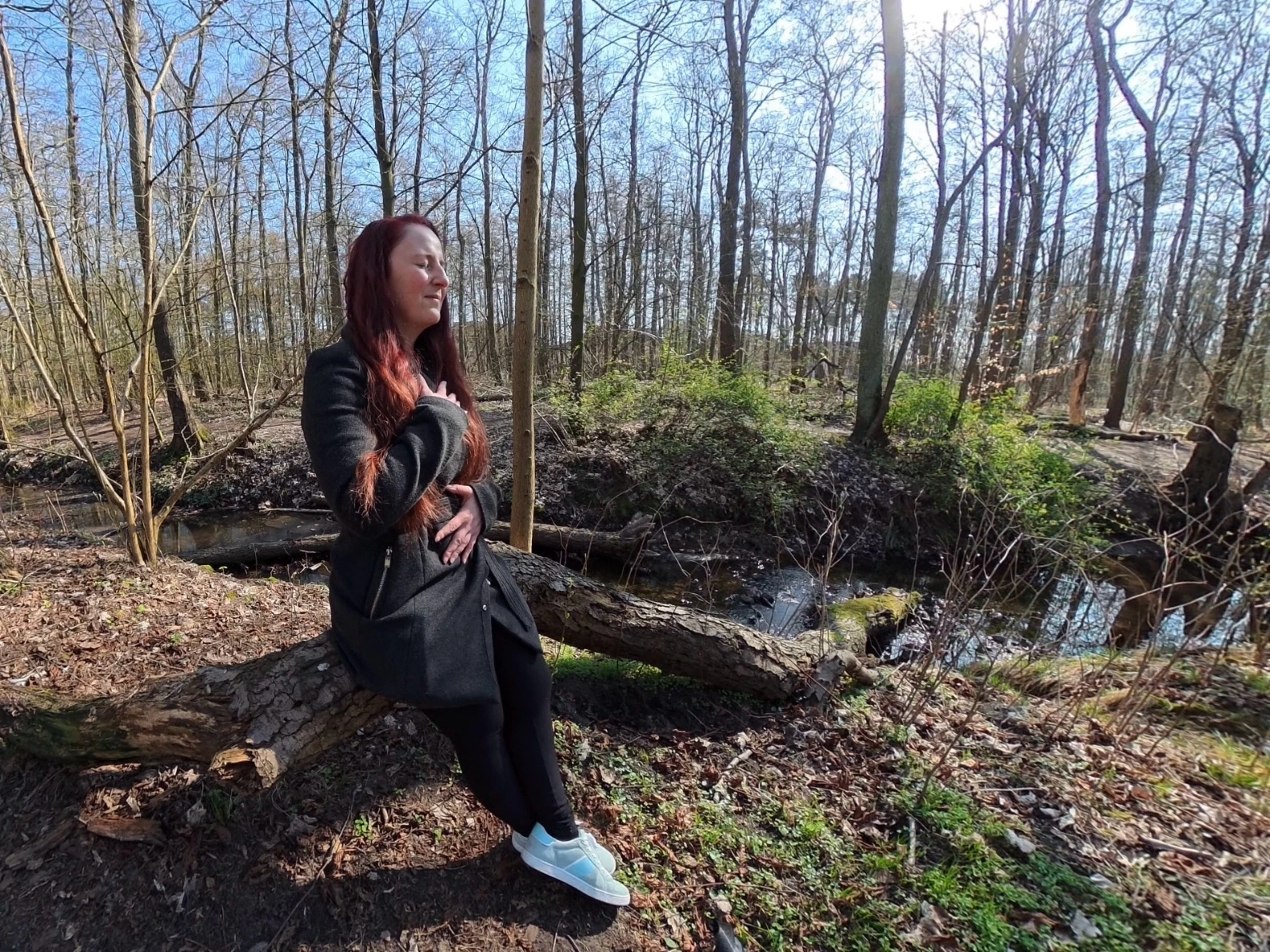 Frau sitzt im Wald mit geschlossenen Augen und legt die H&auml;nde auf Brust und Bauch bei einer Atem&uuml;bung