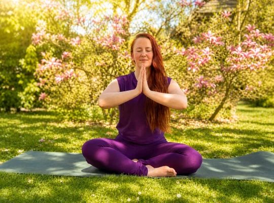 Frau sitzt im Schneidersitz beim Yin Yoga im Garten mit gefalteten H&auml;nden vor der Brust unter bl&uuml;hendem Baum