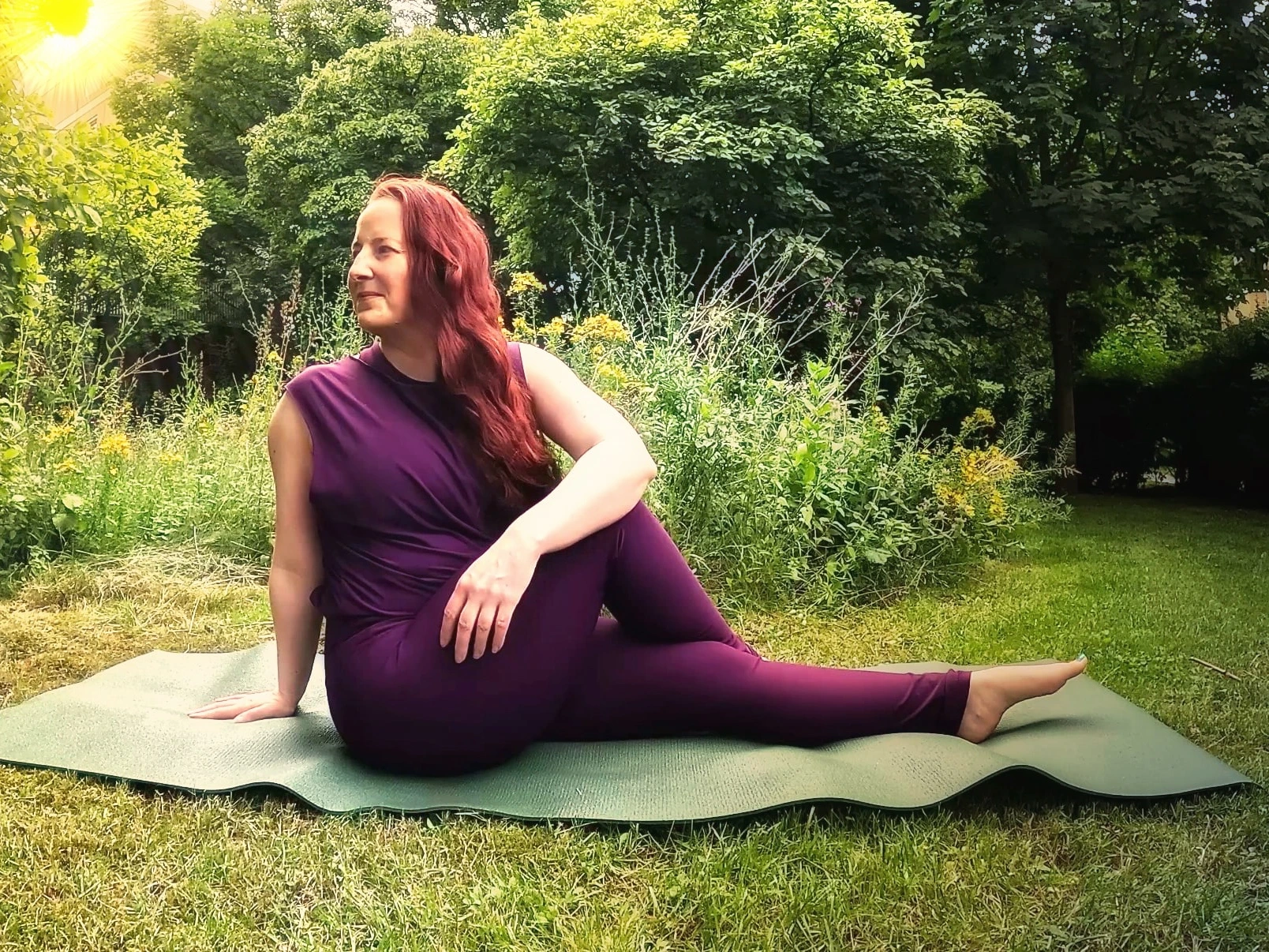 Frau bei einer Yogaübung auf einer Matte im Grünen.