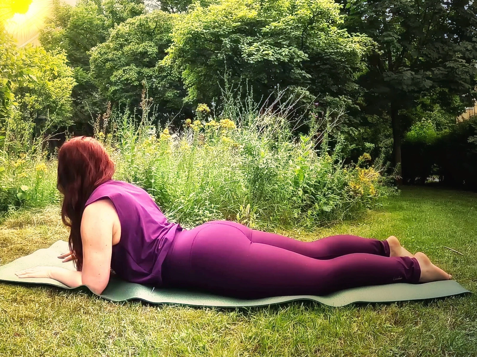 Frau in der Sphinx (Salamba Bhujangasana) auf einer Yogamatte im Garten während einer ruhigen Yin-Yoga-Morgenpraxis.