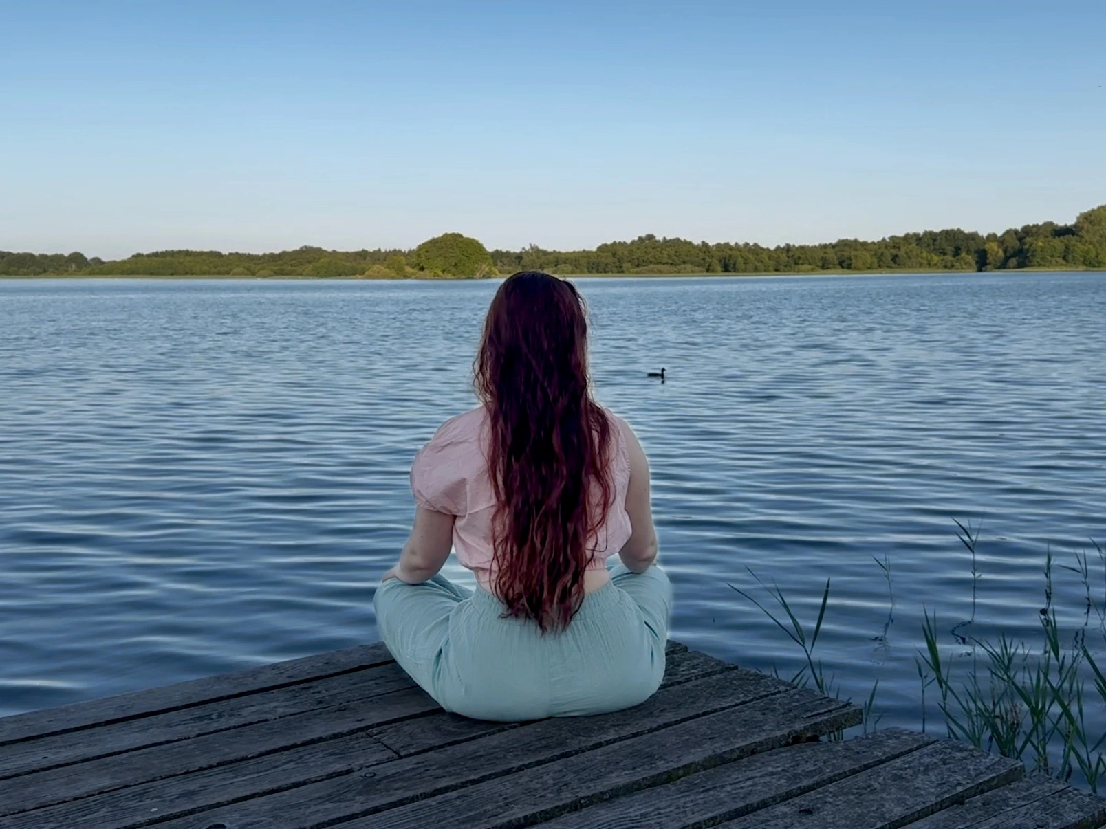 Frau sitzt am Ufer eines Sees und blickt auf das Wasser